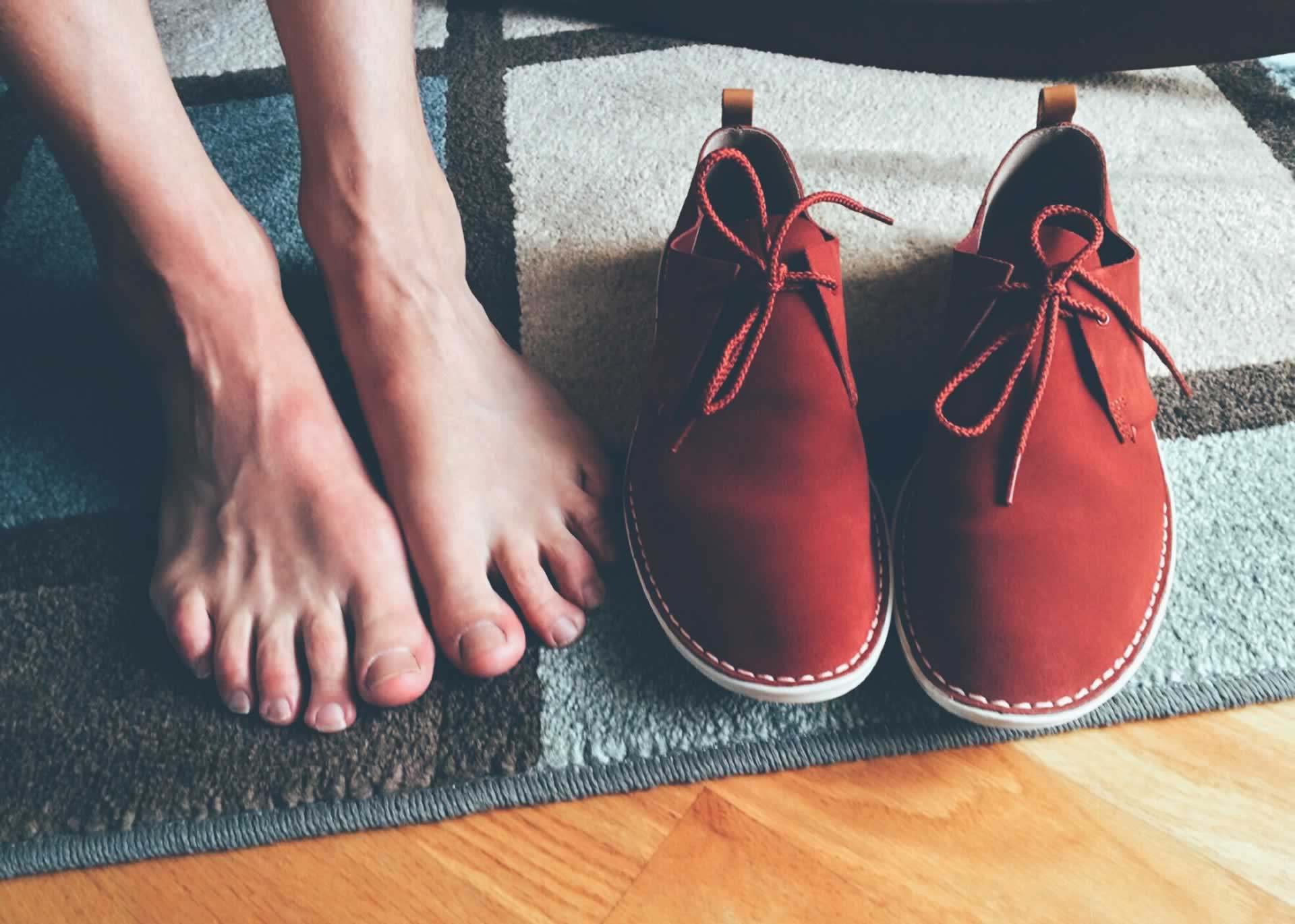 Bare feet resting on a rug beside a pair of red shoes